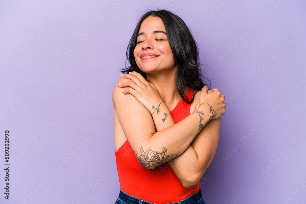 Young hispanic woman isolated on purple background hugs, smiling carefree and happy. - obrazy, fototapety, plakaty 