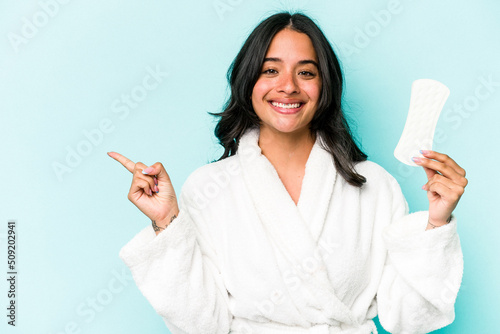 Young caucasian woman holding sanitary napkin isolated on pink background smiling and pointing aside, showing something at blank space.