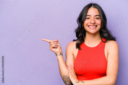 Young hispanic woman isolated on purple background smiling cheerfully pointing with forefinger away.