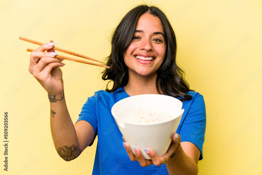 Young hispanic woman eating noodles isolated on yellow background Young hispanic woman eating noodles isolated on yellow background
