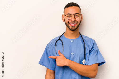 Young hispanic nurse man isolated on white background smiling and pointing aside, showing something at blank space.