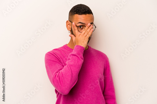 Young hispanic man isolated on white background blink through fingers frightened and nervous.