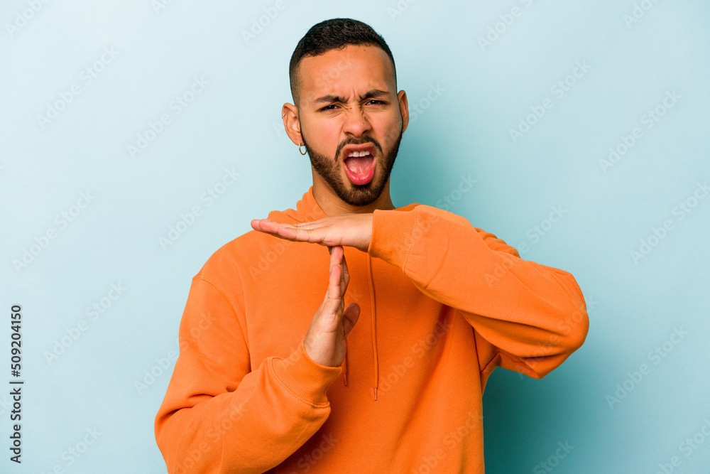 Young hispanic man isolated on blue background showing a timeout gesture.