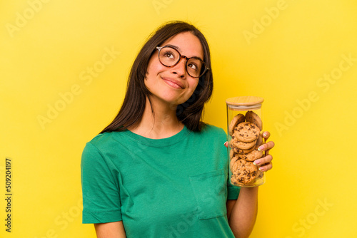 Foto Young hispanic woman holding a cookies jar isolated on yellow background dreamin
