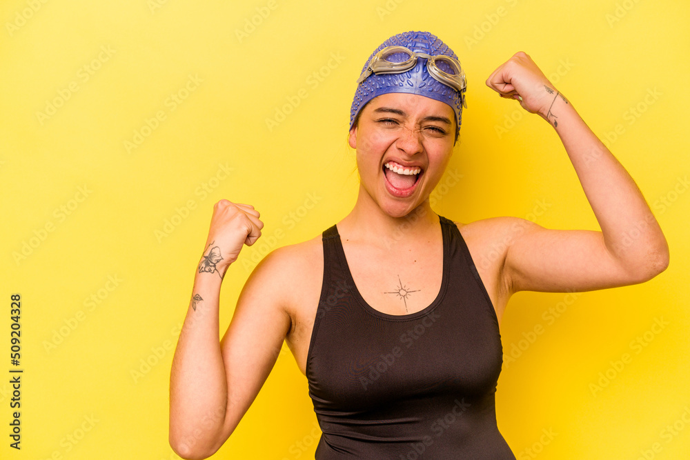 Young swimmer hispanic woman isolated on yellow background raising fist after a victory, winner concept.