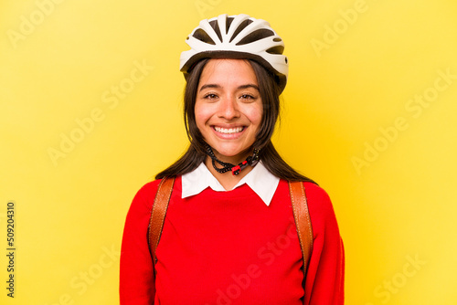 Young student hispanic woman wearing a bike helmet isolated on yellow background happy, smiling and cheerful.