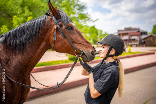 Lovely young woman wearing helmet stroking to her brown horse © dtatiana