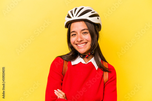 Young student hispanic woman wearing a bike helmet isolated on yellow background laughing and having fun.