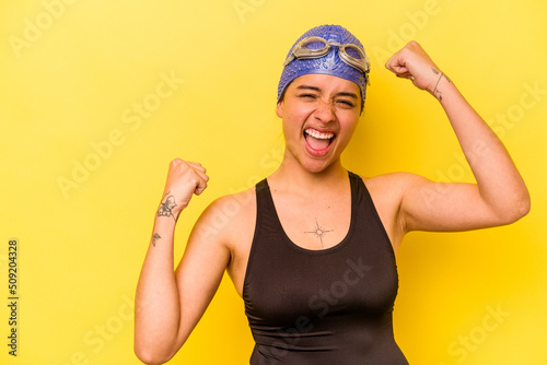 Young swimmer hispanic woman isolated on yellow background raising fist after a victory, winner concept.