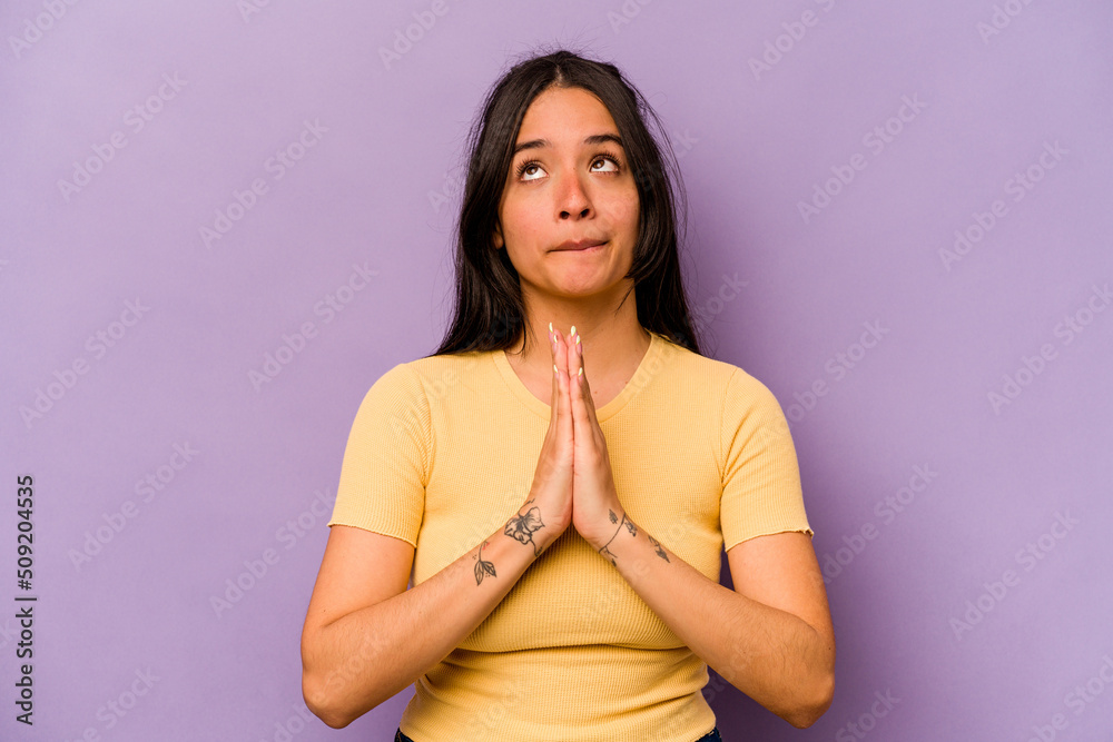 Obraz premium Young hispanic woman isolated on purple background holding hands in pray near mouth, feels confident.