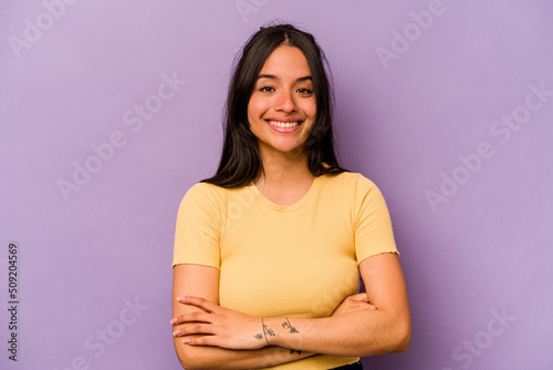 Young hispanic woman isolated on purple background who feels confident, crossing arms with determination.
