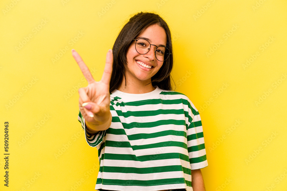Young hispanic woman isolated on yellow background joyful and carefree showing a peace symbol with fingers. Young hispanic woman isolated on yellow background joyful and carefree showing a peace symbol with fingers.