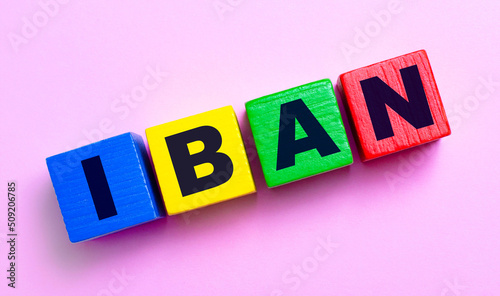 On a light pink background, multi-colored wooden cubes with the text IBAN INTERNATIONAL BANK ACCOUNT NUMBER