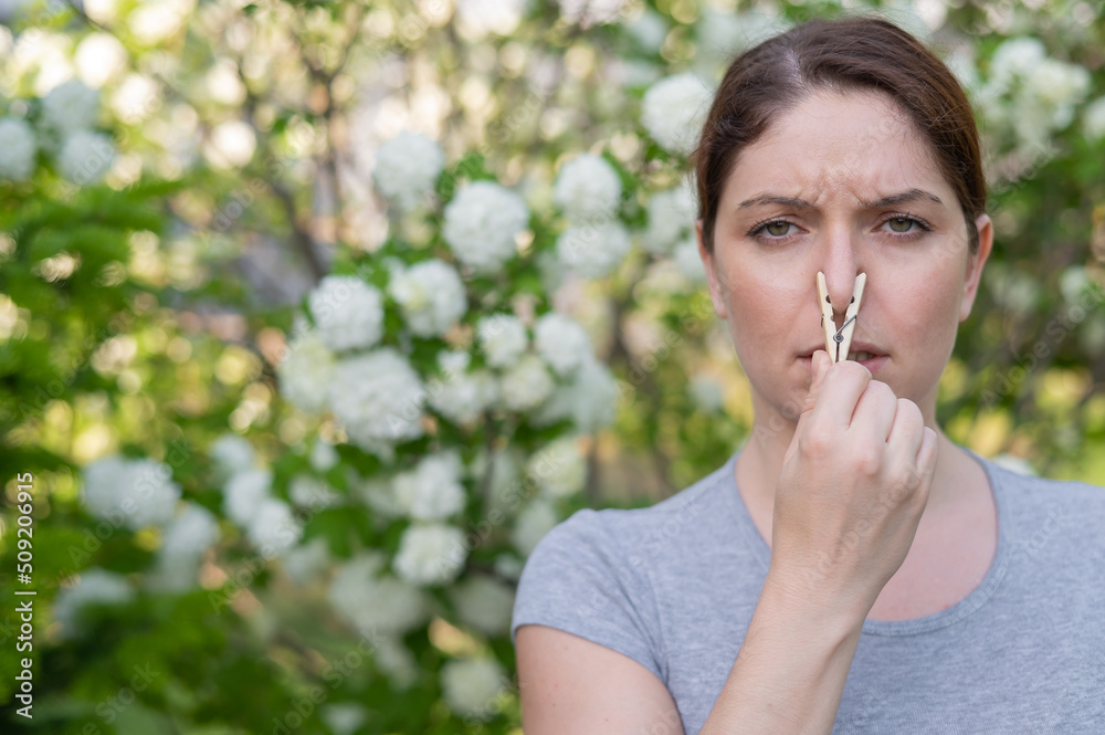 Caucasian woman with a clothespin on her nose on a walk in a blooming park. Caucasian woman with a clothespin on her nose on a walk in a blooming park.