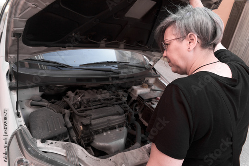 Woman checking the engine of a car with the hood open.