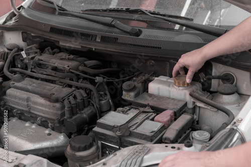 Hands of a woman checking the antifreeze fluid in a car engine.