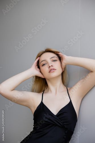 Portrait of fashionable woman in dress touching hair near wall.