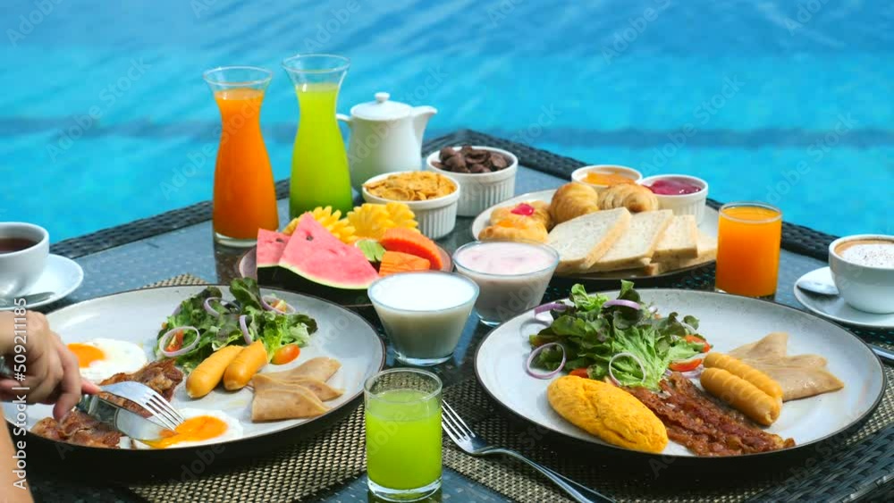 Vacation breakfast table. Woman hands cutting sunny side eggs at luxury restaurant or villa hotel room near the blue swimming pool on tropical holidays. Breakfast for two, romantic, honeymoon travel. Vacation breakfast table. Woman hands cutting sunny side eggs at luxury restaurant or villa hotel room near the blue swimming pool on tropical holidays. Breakfast for two, romantic, honeymoon travel.