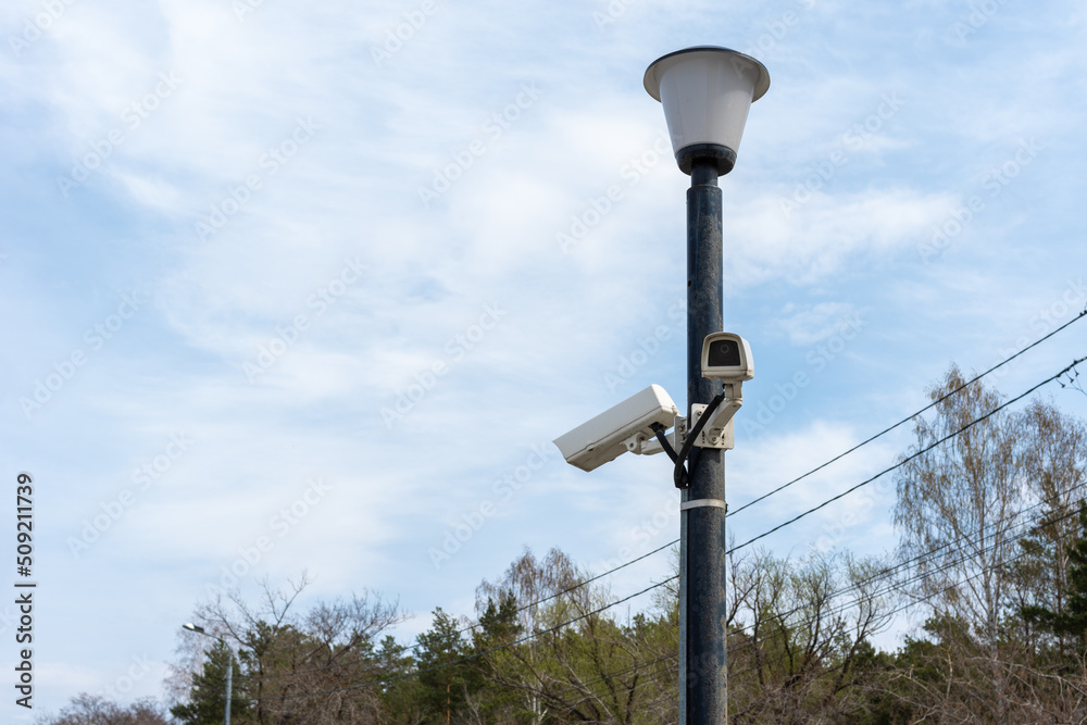 Surveillance cameras mounted on a lamppost at the side of a forest road. security cctv camera. Security in the city. Hidden filming of what is happening. Modern technologies and equipment Surveillance cameras mounted on a lamppost at the side of a forest road. security cctv camera. Security in the city. Hidden filming of what is happening. Modern technologies and equipment