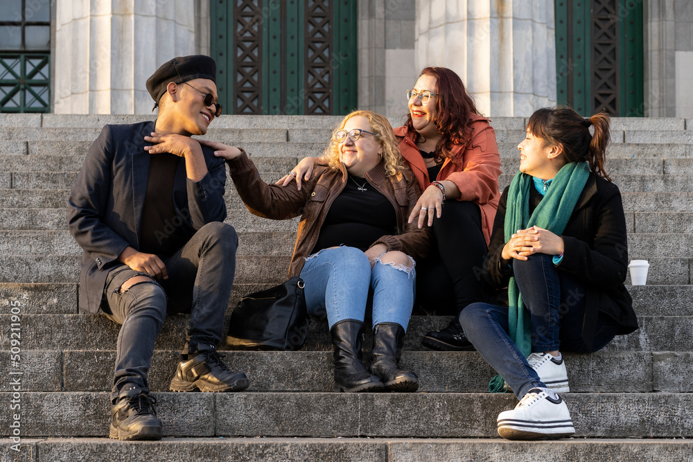 Fototapeta premium Multi ethnic group of friends sitting on some stairs having a good time chatting and laughing