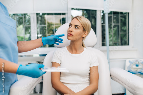 Beautiful and happy blonde woman at beauty medical clinic. She is sitting and talking with female doctor about face aesthetic treatment.