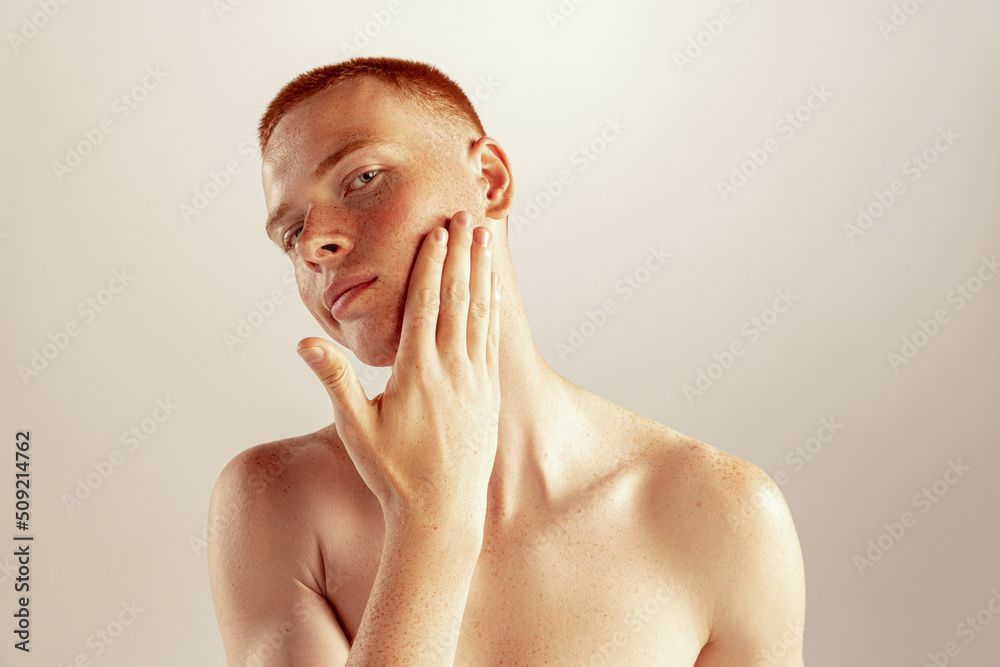 Portrait of young red-haired man with freckles touching cheeks, posing ...