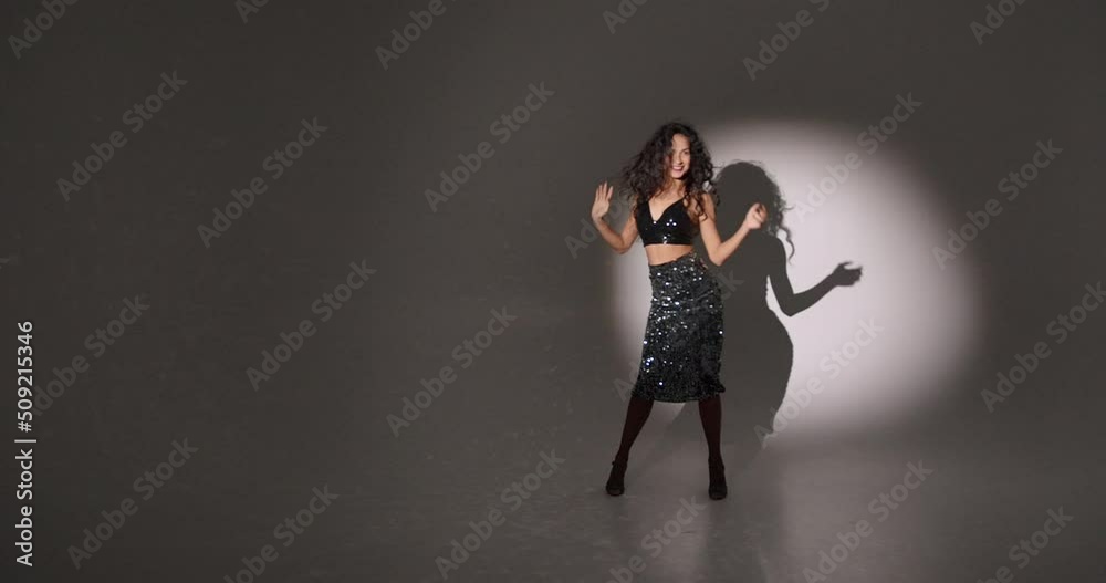 Young woman with curly hair dancing in a dark studio