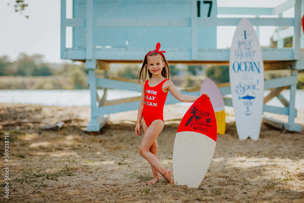 Pretty little girl in red bikini posing with small surfboard like a