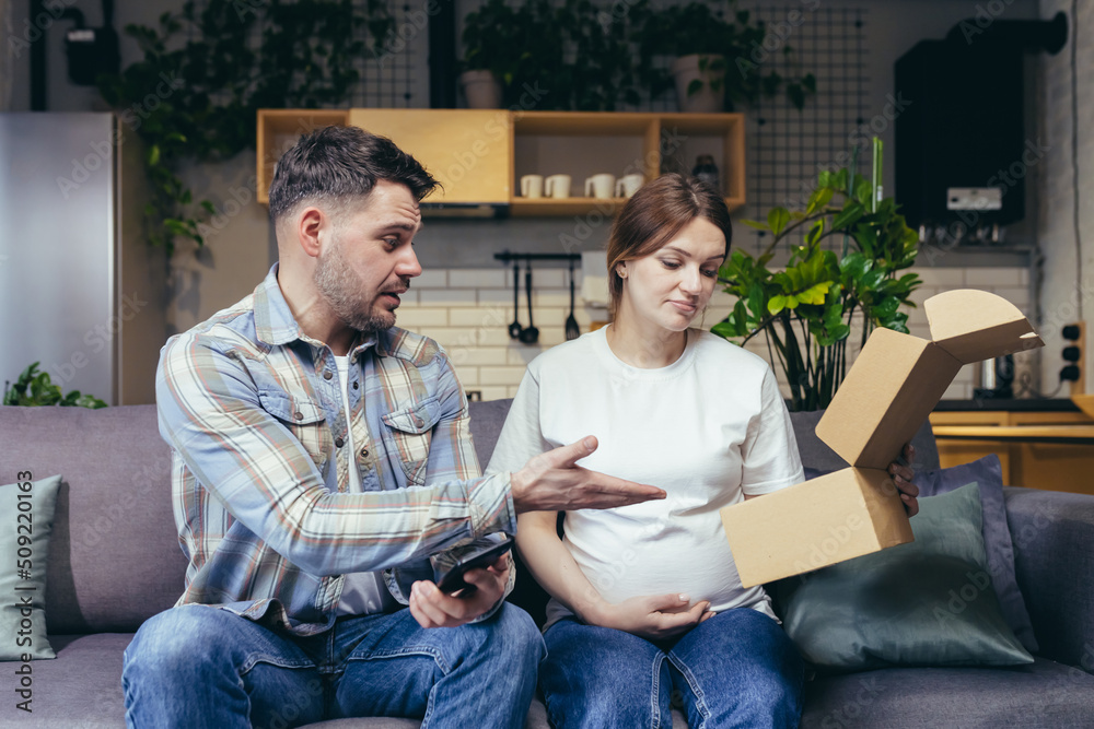 A young family, a pregnant woman and a man accidentally received someone else's parcel. They opened the box, disappointed. Sitting at home on the couch, sad. The man holds his head