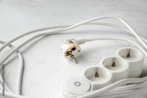 Burnt electric extension cord plug after a short circuit, faulty electrical appliance, gray concrete background, close-up.