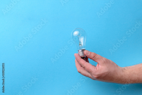 Closeup of hand holding light bulb, isolated on blue background, copy space
