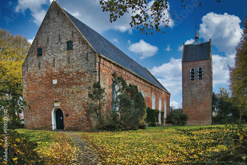 The 12-th century church in the village of Baflo, province of Groningen, the Netherlands, on an autumn day, with fallen leaves in the foreground.
 photo