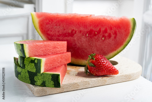 Summer concept, slices of juicy seedless watermelon and strawberry on a cutting board in sunlight.