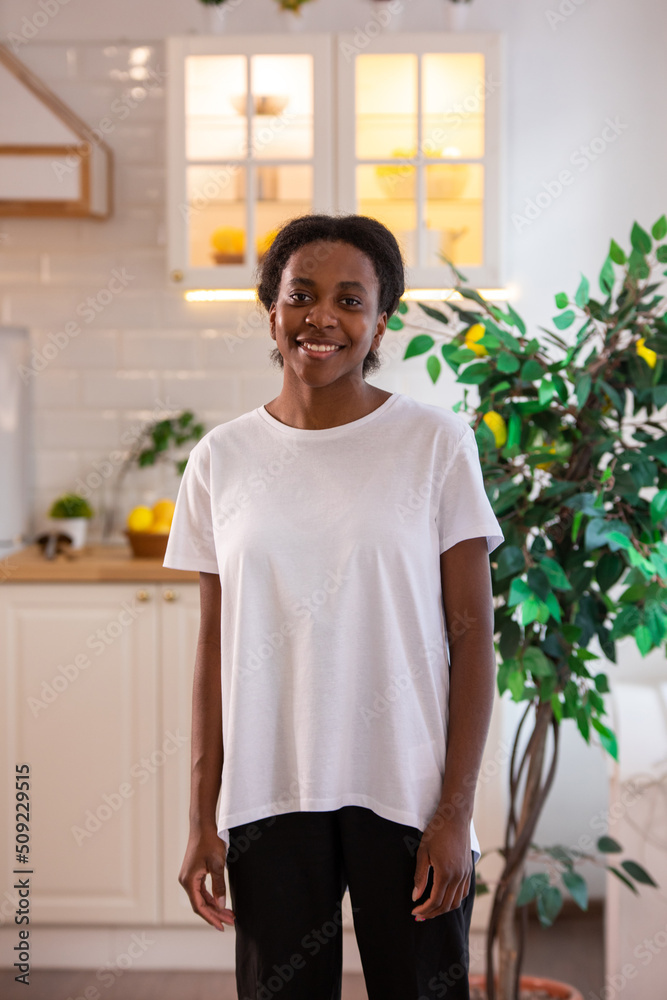 Fototapeta premium African american woman in white t-shirt in the kitchen. Mock-up.