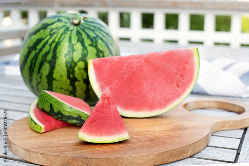 Watermelon and slices on a table on wooden terrace.