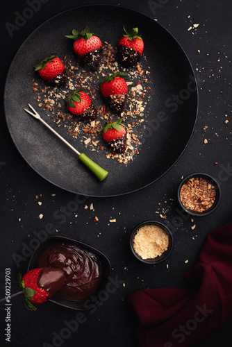 Dessert with chocolate covered strawberries on  black plate on  black background, top view.