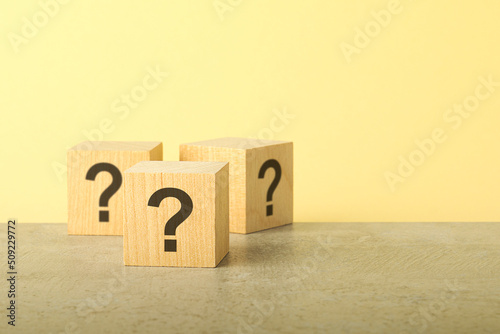 Cube with question mark on wooden background. Space for text