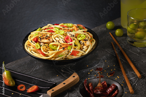 Stir fry noodles with vegetables and chicken in black wok pan. Dark background. Copy space.