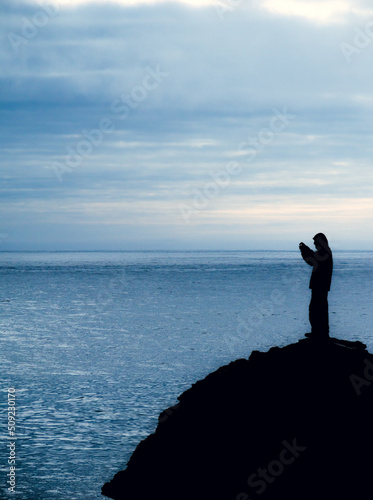 Silueta de hombre con c  mara sobre una roca en primer plano con paisaje del mar de playa en d  a nublado de fondo