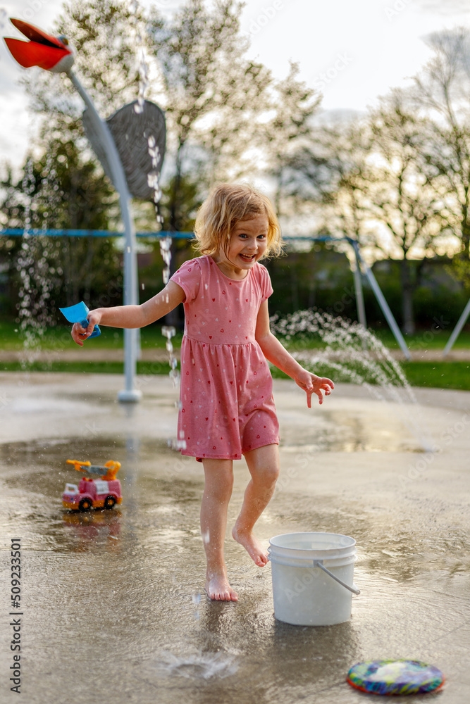 Naklejka premium Happy child playing at splash pad playground in summer. Water park with fountains for children