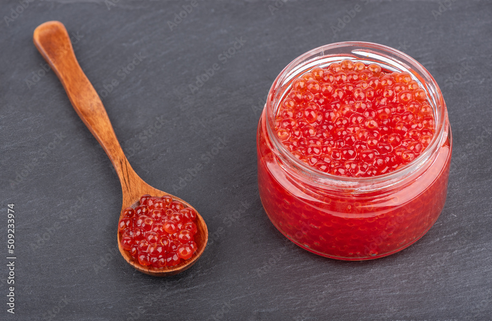 Red caviar in a glass jar and on a wooden spoon.
