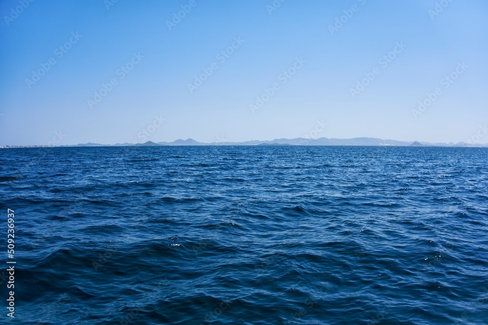 Firm land and mountains seen in the distance from a calm sea on a sunny day with a clear sky and blue sky