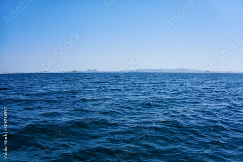 Firm land and mountains seen in the distance from a calm sea on a sunny day with a clear sky and blue sky