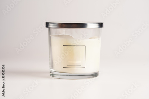 Blank off-white pillar candle in glass jar with label and silver colored lid on white background