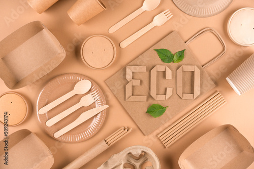 Flat lay image with paper utensils, wooden cutlery and paper word ECO over light brown background. Street food sustainable paper packaging, zero waste packaging concept