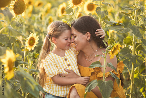 Tender mother and daughter happy together, hugging in nature in a field of yellow sunflowers on a summer day