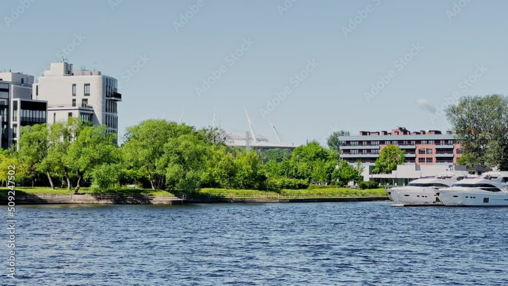 The picturesque river embankment with a residential luxury house at clear weather, mega yachts at the pier of the yacht club in sunny weather
