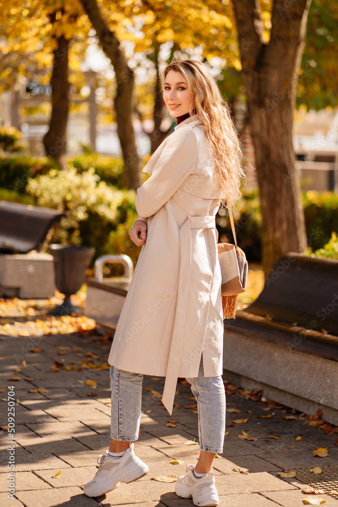 beautiful blonde student or businesswoman in a coat walks down an autumn street.