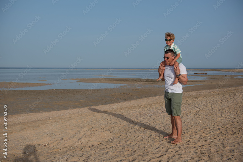 Child sits on father's shoulders on the beach. unchanged, family, lifestyle, togetherness, enjoyment and vacation concept.