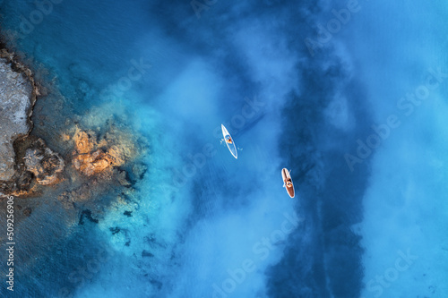 Fototapeta Naklejka Na Ścianę i Meble -  Aerial view of people on floating kayaks on blue sea, rocky coast, trees at sunrise in summer. Blue lagoon, Oludeniz, Turkey. Tropical landscape. Sup boards on clear water. Top view of canoe. Tourism